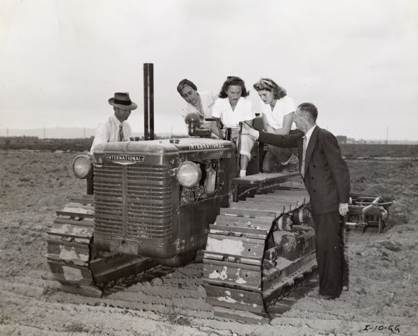 Lillian A. Heinrichs, Lucille Eltiste, and Esther Goubert receive instruction from H.E. des Granges during "Tractorette" class while Wesley Kollehorst, field instructor, looks on. The original caption reads: "Here is <i>[sic]</i> three Tractorettes in the Santa Ana, Calif. Harvester Dealer, August Eltiste's Tractorette class getting some first-hand instruction before their final field test from H.E. des Granges, Diesel Instructor for Fullerton Junior-College and volunteer Tractorette instructor.  Left to right are, Wesley Kollehorst, field instructor; Mrs. Lillian A. Heinrichs, Lucille Eltiste and Esther Goubert."