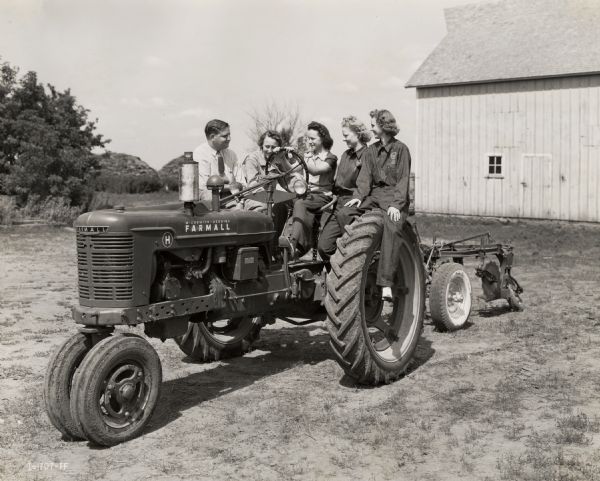 "Tractorettes" pose with their instructor, McCormick-Deering salesmen Robert L. McCaffrey, on a Farmall H tractor.