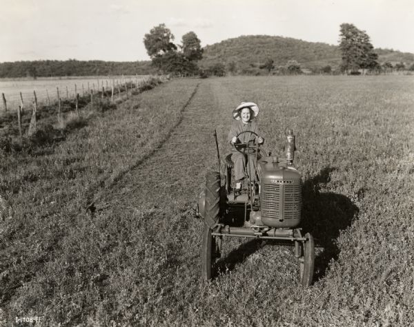 Mrs. Beulah Ogden, a participant in the "Tractorette" class organized by the Blanchard Motor Company, rides a Farmall tractor through an 88-acre farm owned by Mrs. Helene George.