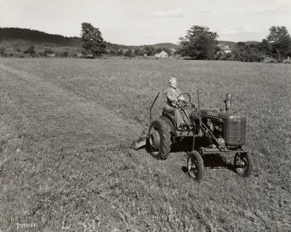 Slightly elevated view of Mrs. Helene George driving a Farmall A tractor as part of a "Tractorette" class organized by the Blanchard Motor Company. The class took place on Mrs. George's 88-acre farm.