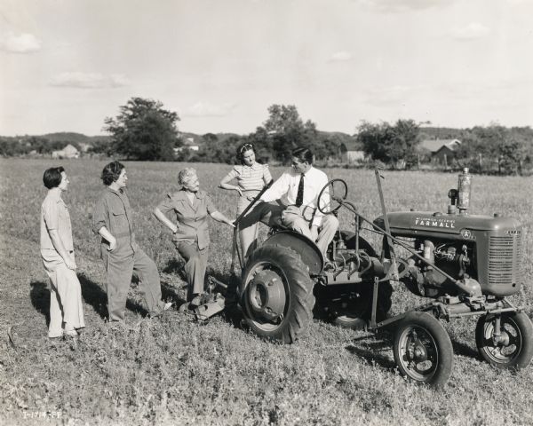 A group of "Tractorette" participants are looking on as their teacher, L.J. DeMars, assistant manager of the Blanchard Motor Company in Springfield, is instructing them from a Farmall A tractor. The class took place on the 88-acre farm of Mrs. Helene George.