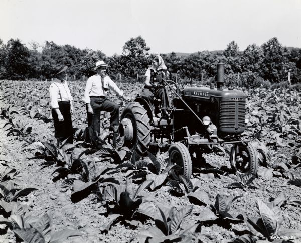 Mrs. Kathryn Mann of Columbia, Pennsylvania, sits on a Farmall A tractor while Walter Dupes, salesman for J.B. Hostetter & Sons of Mount Joy, Pennsylvania, and R.C. Northamer, assistant manager at Boston, stand beside her. Mrs. Mann was likely taking part in International Harvester's wartime "Tractorette" program. The original caption reads: "Pretty Mrs. Kathryn Mann, Columbia, Pennsylvania, is typical of the many young farmer wives who are pitching in as tractor operators these war days and thus helping keep up food production. The crop was tobacco."