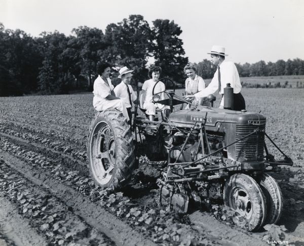 Mrs. John T. Shea, Mary Elma Riddell, and Mrs. John R. Riddell, participants in "Tractorette" class, are posing around a Farmall H tractor with J.S. Inman, farm equipment manager of Hinton & Hutton, and Floyd Sherrod, branch manager.