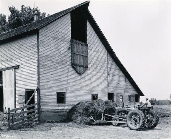 Donald Jarvis uses a Farmall H tractor to stack hay outside a barn.