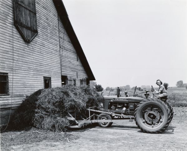 Muriel Thomas of Sperry, Idaho, uses a Farmall H tractor to stack hay outside of a barn. Ms. Thomas may have taken part in International Harvester's wartime "Tractorette" program.