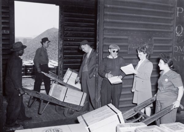 A group of men and women load wooden crates onto a boxcar at International Harvester's Tractor Works (factory).