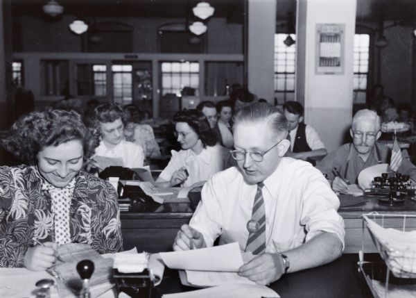 A woman and man are sitting side by side to look over paperwork in an office at International Harvester's Tractor Works.