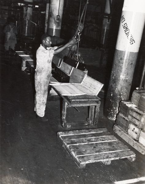 A factory worker is using a pulley system to move a part at International Harvester's Tractor Works.