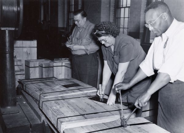A woman and two men work with wooden crates at International Harvester's Tractor Works (factory).