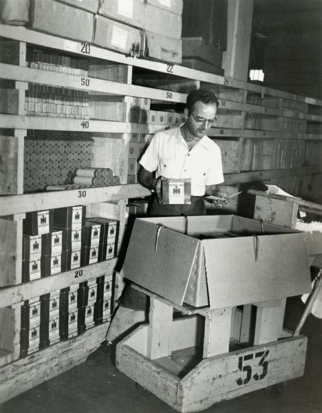 Factory worker Charles Coseniro(?) examines the contents of a box in a warehouse at International Harvester's Tractor Works.
