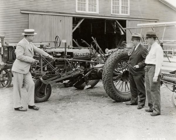 Three men stand around a Farmall F-12 tractor outside of a storage building, possibly at the Gonigam-Bass Company. The men may be International Harvester dealers or salesmen.