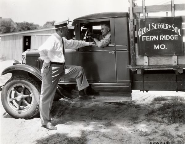 A man speaks to the driver of an International truck labeled "Geo. J. Seeger & Son; Fern Ridge, MO."
