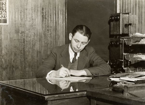 George H. Kaelin, in charge of farm machinery sales at Long Island Produce and Fertilizer Co., Inc., sits behind a desk. Long Island Produce and Fertlizer Co. was likely an International Harvester dealership.