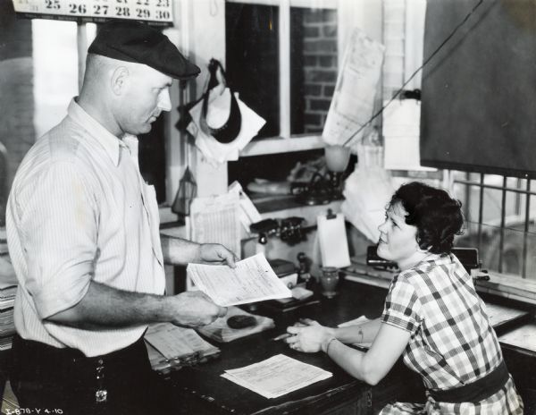 Dorothy Edwards sits at a desk while her husband, H.L. Edwards, stands beside her. The couple were operators of Edwards Truck Line and owned six International trucks employed in long-distance hauling.