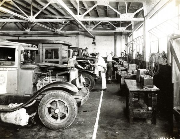 Men work on trucks in the garage at Quinn R. Barton, Inc., an International Harvester dealership. The men in the photograph include mechanics Ralph Randall, O.L. Royal, J.R. Snyder, and C.J. Tucker, and shop foreman R.L. Ray.