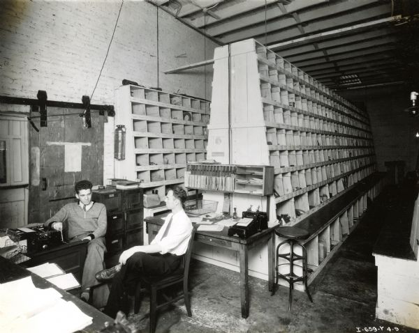 F.C. Rogers, parts manager, and H.C. Rogers, assistant, sit in the parts room of Quinn R. Barton, Inc., an International Harvester dealership.