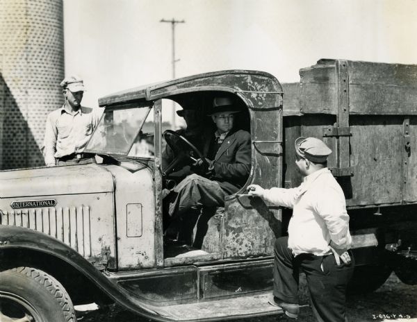 L. Garrett sits in the driver's seat of an International Model A-5 truck with a 156-inch wheelbase used by the City of Jacksonville Garage. L. Wadsworth, transportation foreman of the Street Cleaning Department, stands next to Garrett.