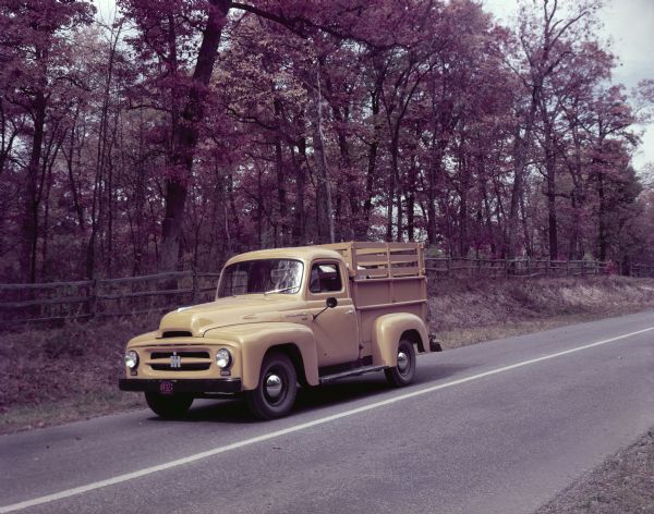 Color photograph of an International Harvester standard model R-110 truck with a pickup body and ADA-RAK travels down a wooded road.