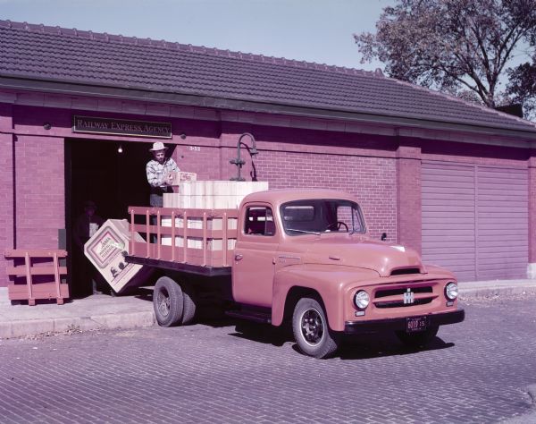 View of a man standing on the back of an International R-120 truck with a stake body to unload boxes of Whip salad dressing.