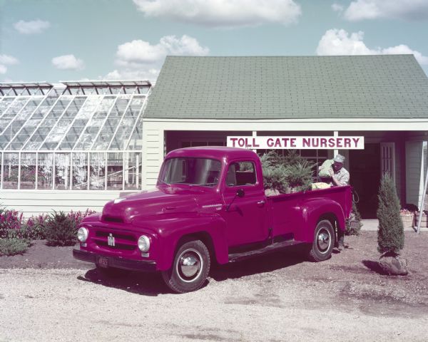 Color photograph of a man unloading a burlap bag onto the back of an International R-120 pickup truck in front of "Toll Gate Nursery."