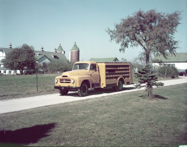 Color photograph of an International R-160 truck with a closed deck and bottler's body parked in front of a large farm building.