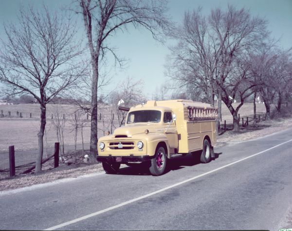 Color photograph of an International R-170 truck with a service utility body parked along the side of a road. A metal ladder is attached to the side of the truck.