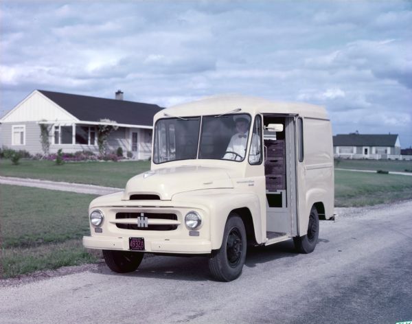 View of an International RA-140 milk delivery truck parked along the side of the road, with a milkman in the driver's seat.