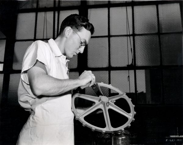 A wood pattern-maker apprentice at McCormick Works (factory) shellacs a sprocket wheel pattern.