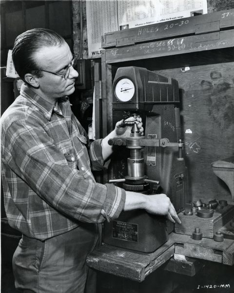 An factory worker at McCormick Works uses a Rockwell Hardness Tester to check ledger plates.