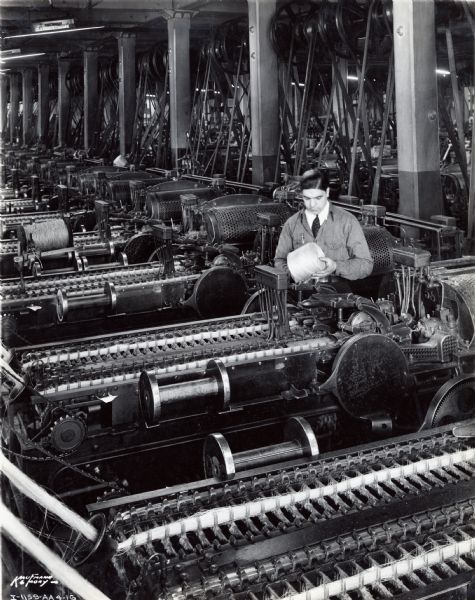 A man at McCormick Works Twine Mill stands in between various rows of machinery to inspect a ball of twine.