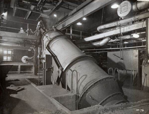 Factory workers at McCormick Works charge an 8-ton Brackelsberg Furnace. The original caption reads: "10 charging buckets holding 1,600 lbs. each are moved into charging position by a motor-operated car and tilted by means of an air hoist. Note pulverized coal burner swung out of position."
