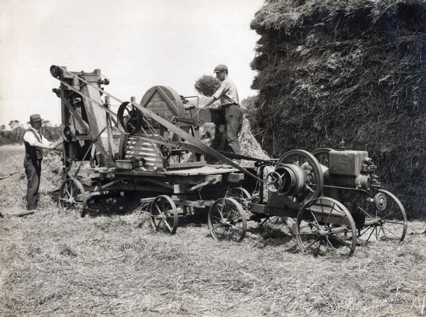 Two farmers use an International Harvester engine and portable chaff cutter on an Australian farm.