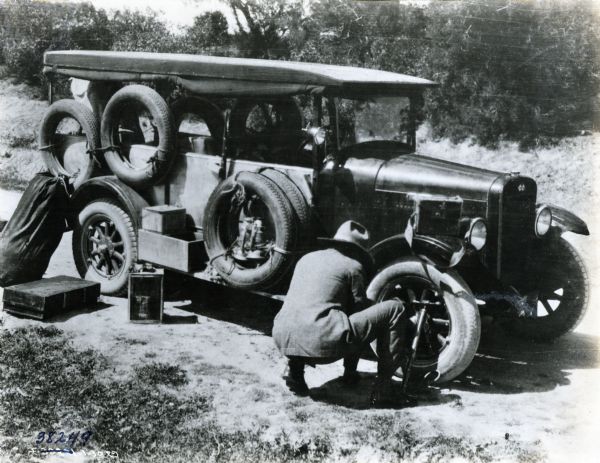 A man stoops to change the tire of an International Special Delivery truck by the side of an African road. The truck was part of an expedition sponsored by International Harvester to cross Africa. The truck later became known as the "truck that crossed the Sahara."