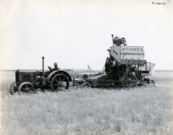 A farmer is using a McCormick 15-30 tractor and No. 11 harvester-thresher (combine) in an unspecified non-United States location. The original caption reads: "Note that the machines have been changed over from McCormick-Deering to McCormick for foreign use."
