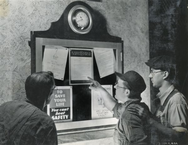 Factory workers looking at safety posters on a bulletin board at the McCormick Works.
