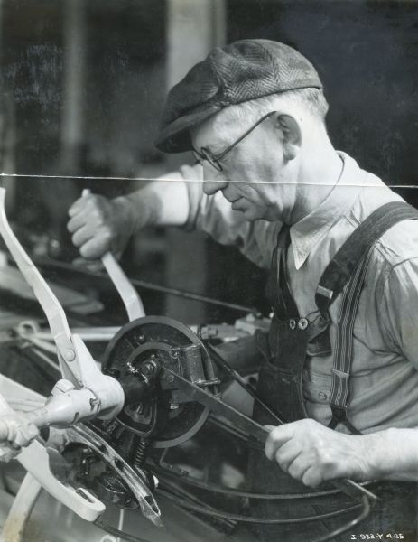 John Kiecol, dean of the 40-year special safety committeemen, works in the Quality Inspection Department at an International Harvester factory (most likely McCormick Works). The original caption reads: "John Kiecol, dean of the 40-year special safety committeemen, as he goes about his daily work in one of many divisions of the Quality inspection department. His duties consist of selecting at random binders, spreaders, and other machines already crated and packed for shipment, setting them up, operating them, checking the parts for 'fit' and the whole assembly for smooth  and efficient operation. John's service totals more than 44 years."