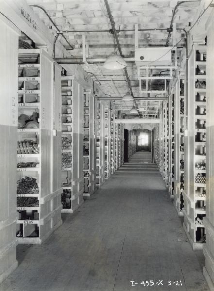 View down an aisle with rows of shelves containing parts for agricultural implements at the McCormick Works (factory).