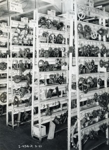 Several storage racks stocked with hanging gears and machine parts fill a room at the McCormick Works (factory).