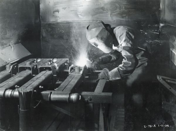 Factory worker wearing a protective mask while welding metal at the McCormick Works.