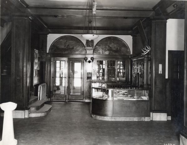 Lobby and cashier's desk in the McCormick Works Club House. In the center is a set of double doors. On the left is a flight of stairs. The Club House was designed for recreational use by factory employees.