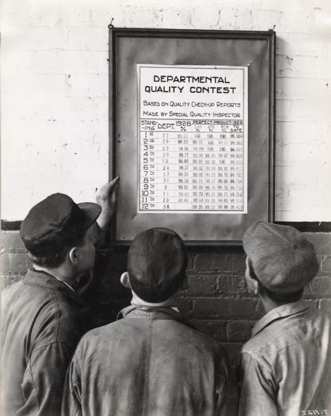 Three factory workers look at a poster entitled "Departmental Quality Contest" at the McCormick Works.