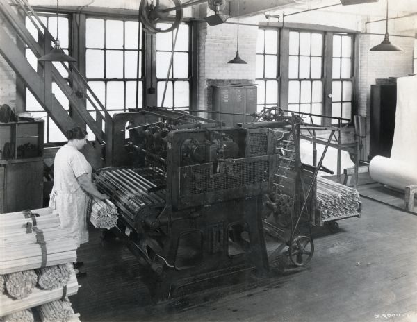 A female factory worker bundles wooden spindles with a machine at the McCormick Works.