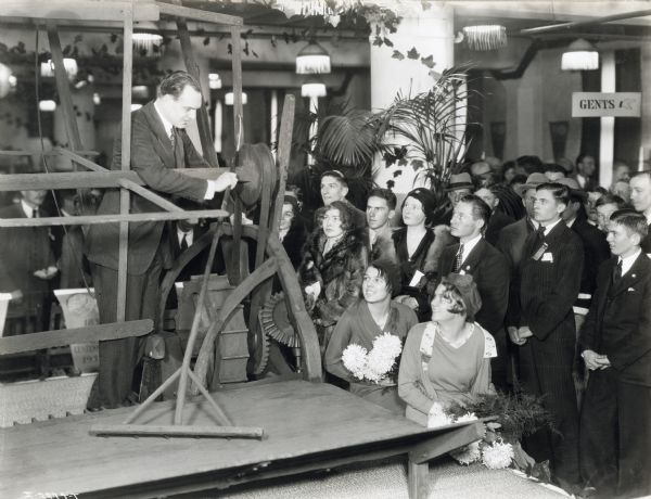 A man, possibly Cyrus McCormick III, demonstrating a reaper replica to a group of onlooking 4-H Club members.
