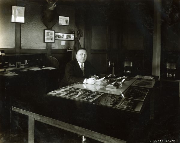 William Clay Ford Sr.(?) sits behind a desk in an office. Mr. Ford may have been an International dealer.