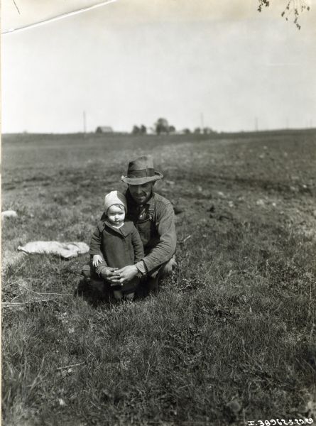 Joe Althoff crouches in a field with arms around his young son.