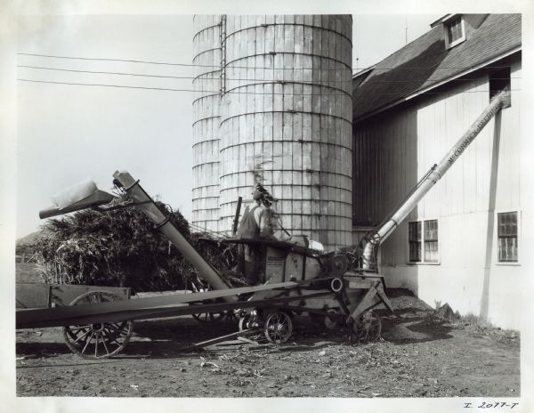 Robert Romley uses a steel husker and shredder near a silo and barn on his farm.