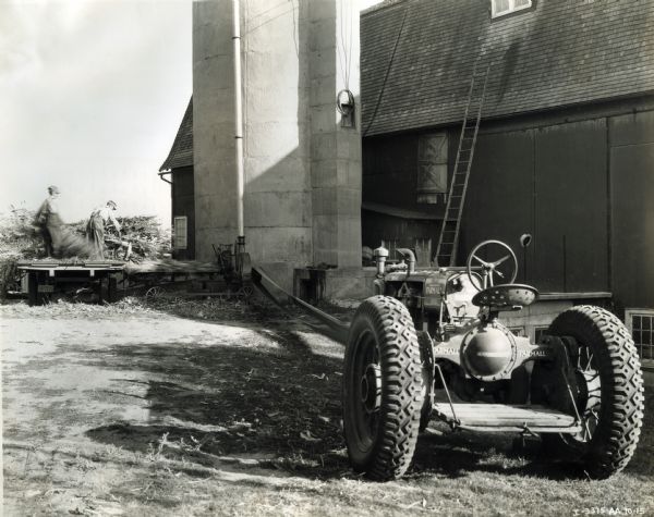 Two farmers use a Farmall "F-20" tractor and a No. 12-C ensilage cutter to complete work on a farm.