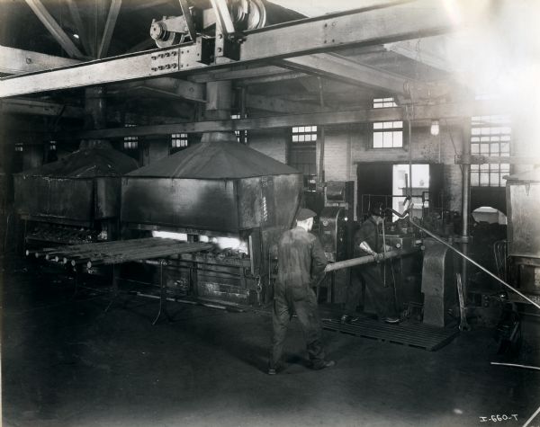 Factory workers lead a long wooden or metal cylinder through a machine at International Harvester's West Pullman Works.