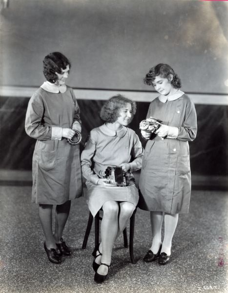 Three women are posing while holding metal parts manufactured at West Pullman Works.