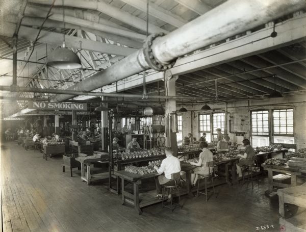 Male and female factory workers sitting at tables at West Pullman Works. A large sign hanging from a pipe reads: "No Smoking".